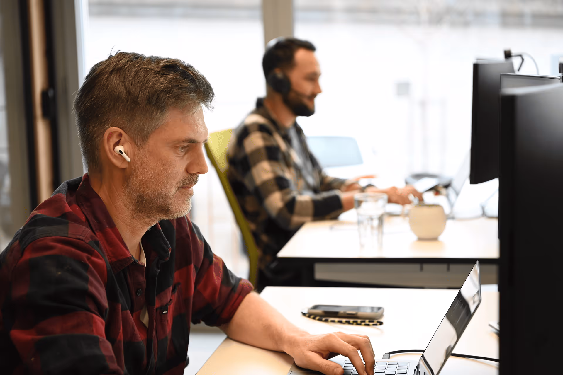 Zwei Männer arbeiten konzentriert an Laptops und Monitor im Grossraumbüro