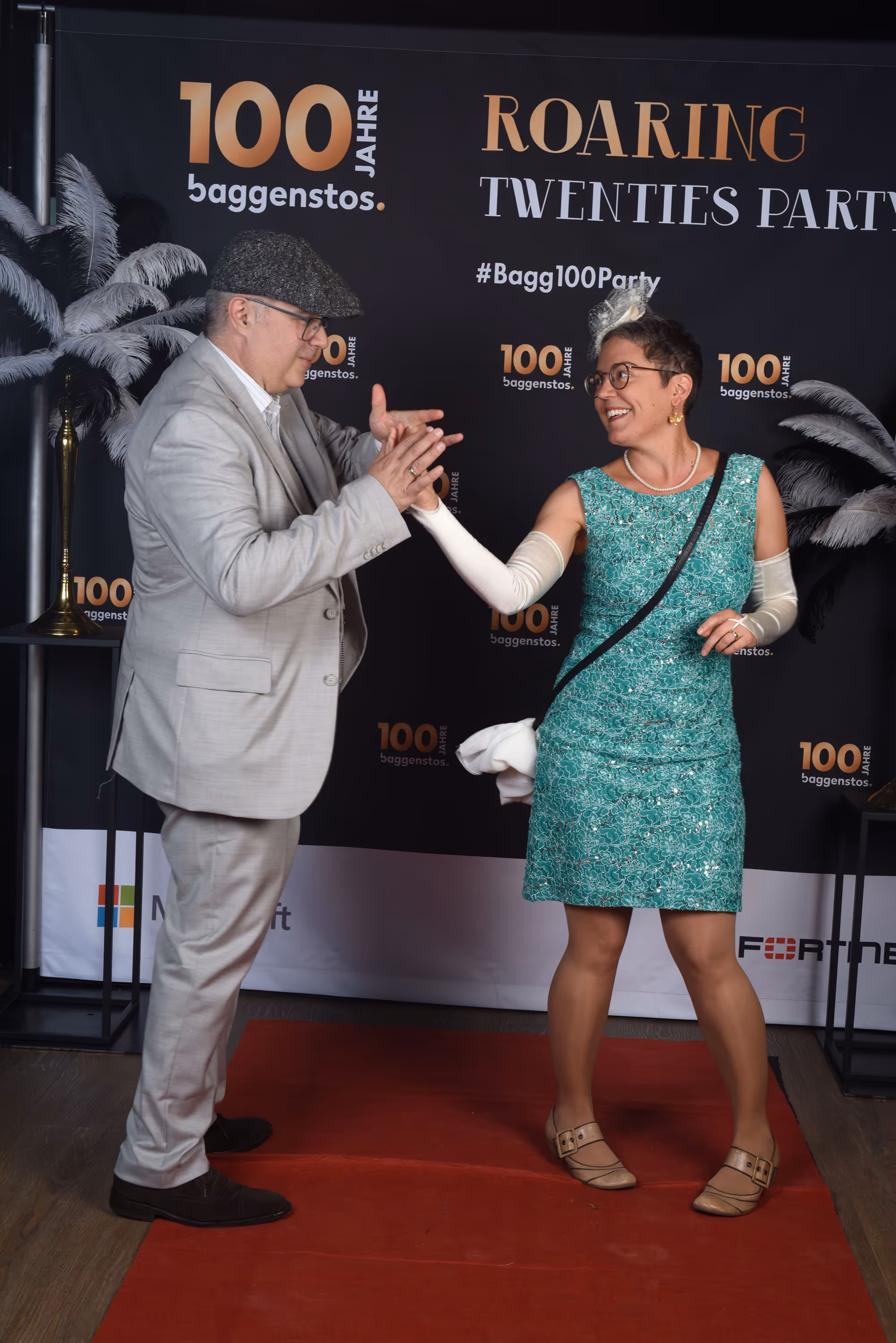 Tanzendes Paar in 20er-Jahre-Outfits vor Fotowand mit Schriftzug Roaring Twenties Party.