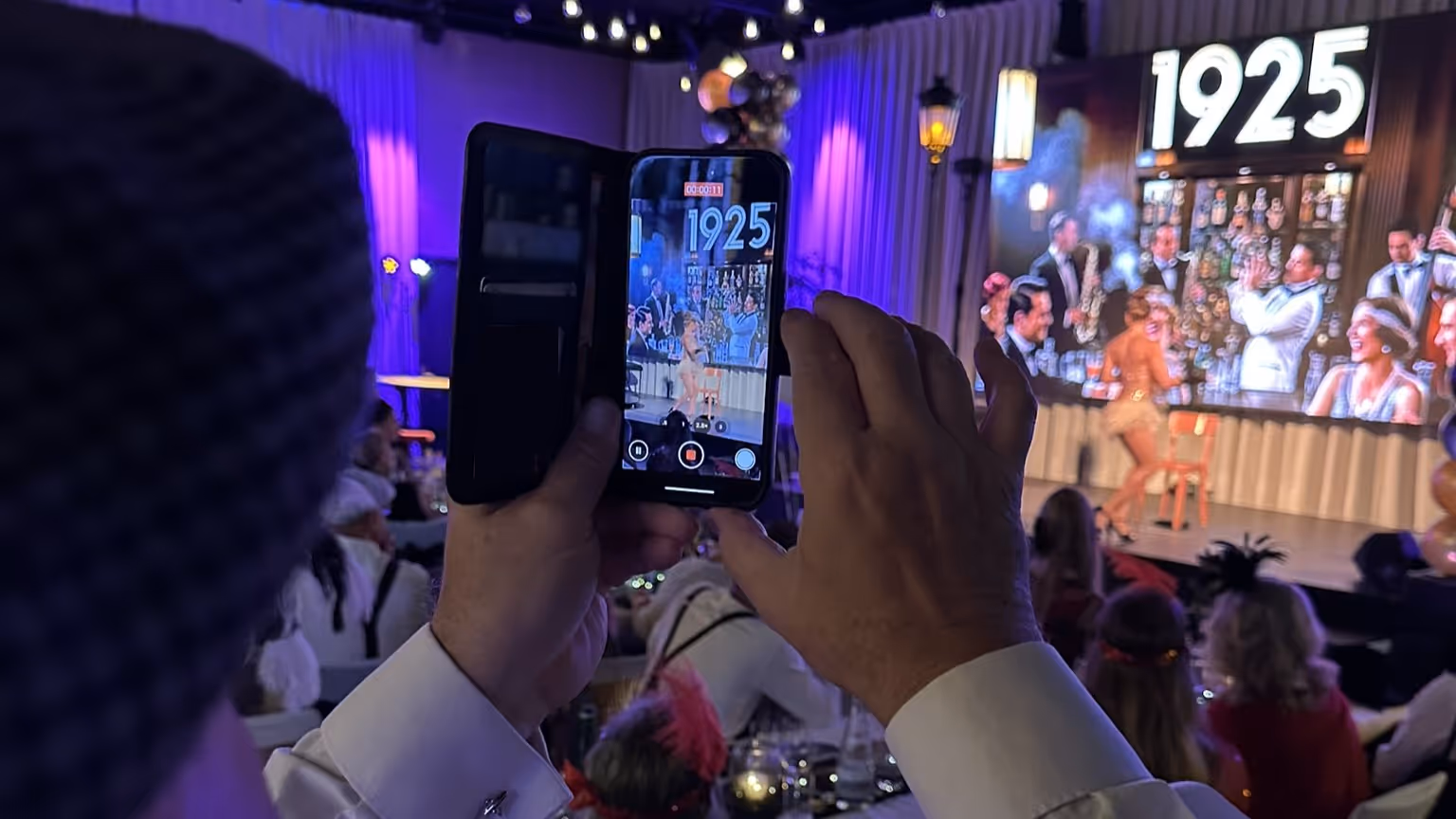 Gast filmt mit dem Smartphone eine Bühnenshow vor leuchtender Kulisse mit der Zahl 1925