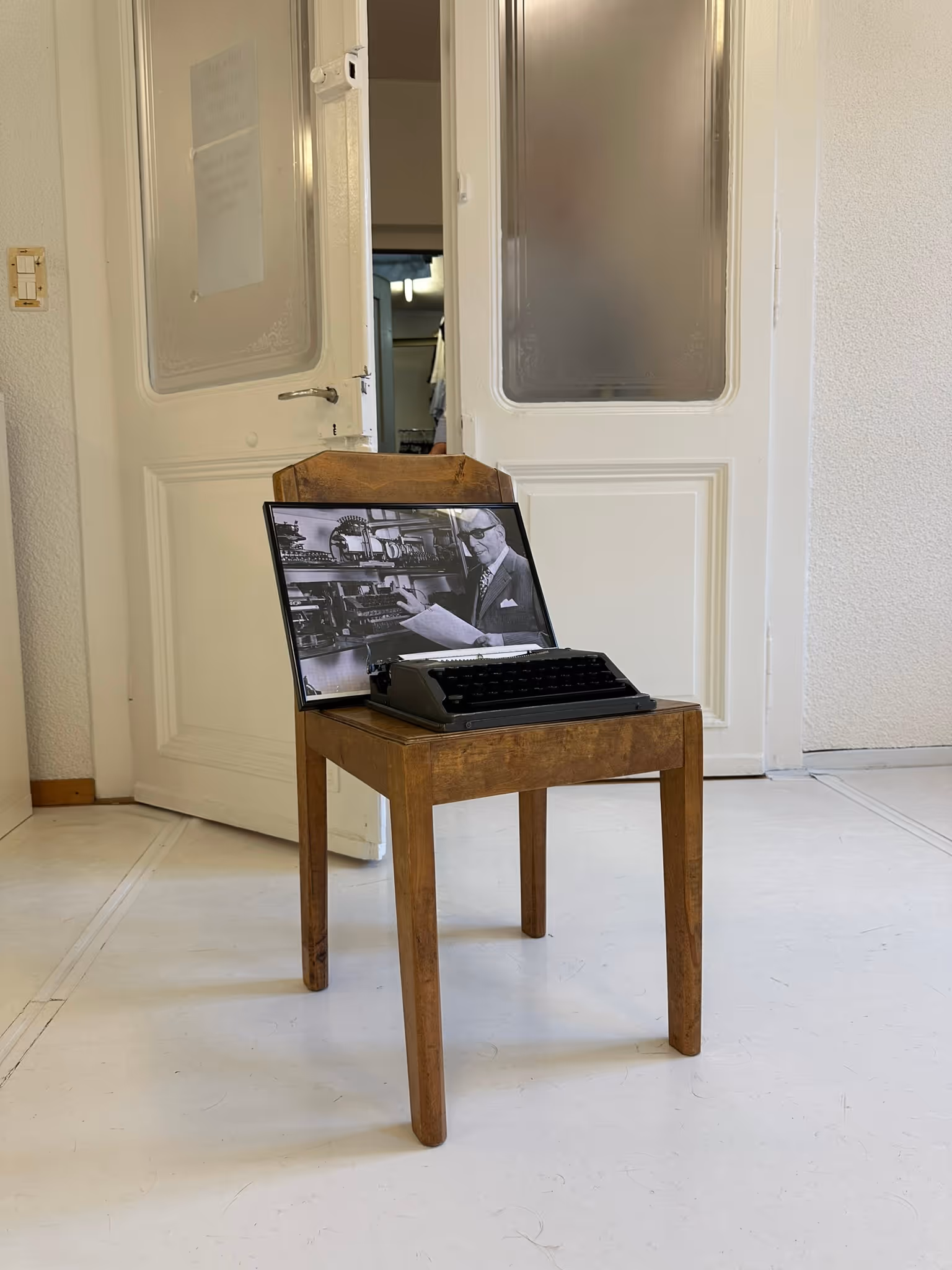 Alter Holzstuhl in hellem Raum mit gerahmtem Schwarz-Weiss-Foto eines Mannes an der Schreibmaschine.
