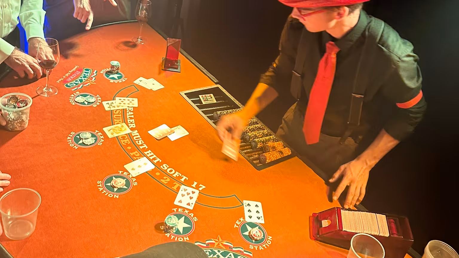 Croupier mit roter Krawatte und Hut teilt Karten an einem Blackjack-Tisch aus