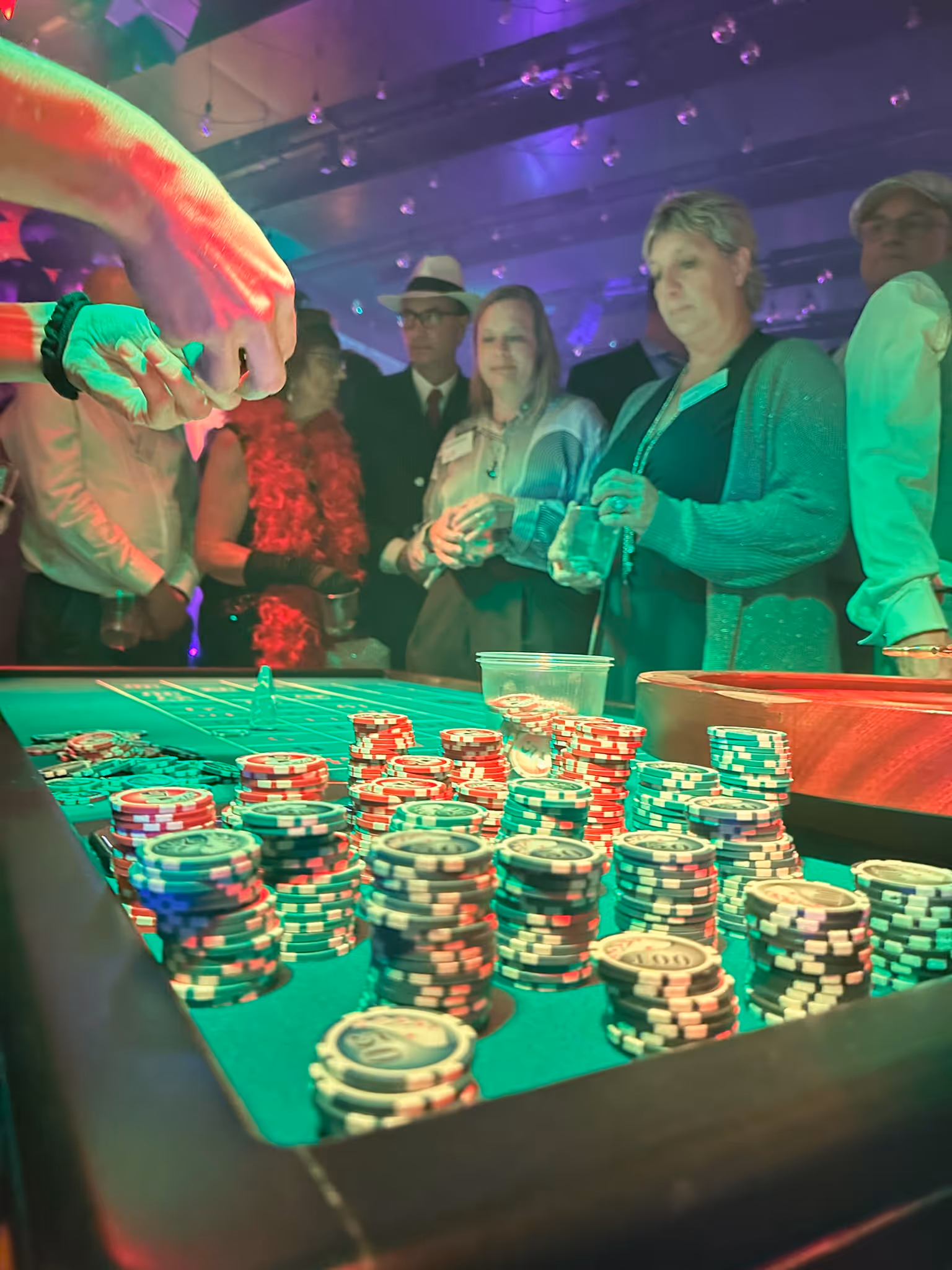 Gäste stehen um einen Roulette-Tisch mit Spielchips an einem stimmungsvoll beleuchteten Casino-Abend