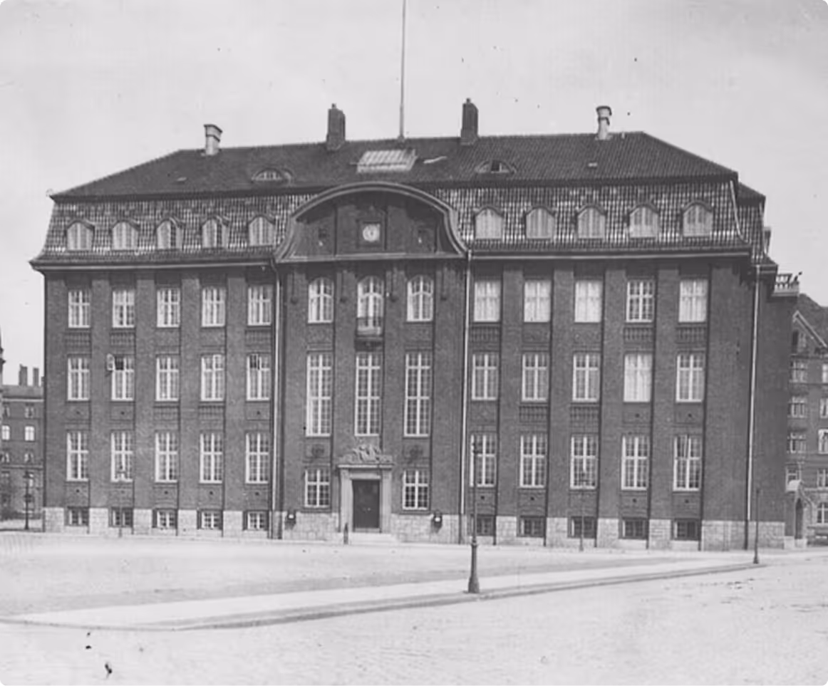 Historic black and white photo of a large multi-story brick building with numerous windows and a central arched entrance.