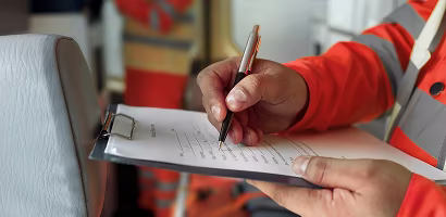 Person wearing a safety vest writing on a clipboard with a pen.