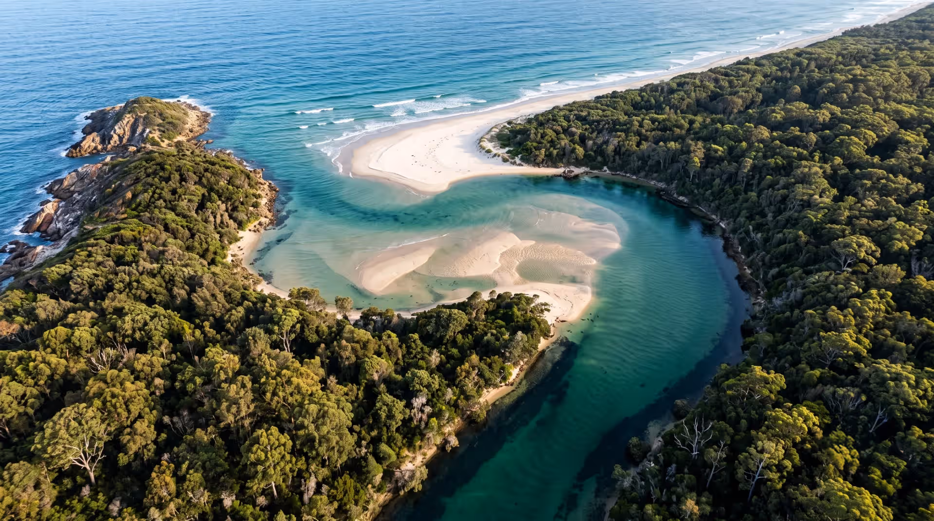 Aerial view of a river flowing into the ocean, surrounded by lush green forest and sandy beaches.