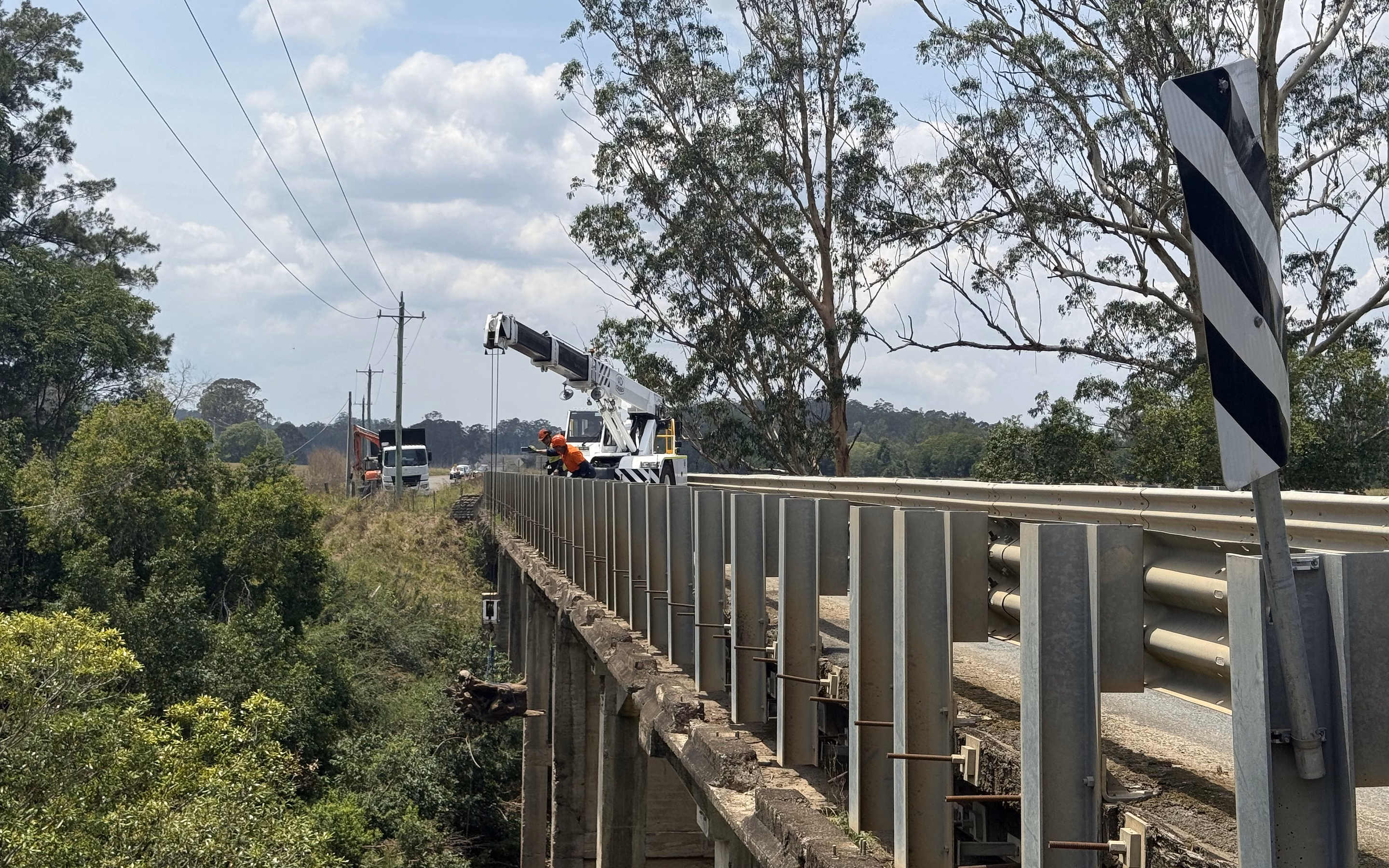 Crane truck and MidCoast Tree Solutions crew removing a tree from a rural river bridge