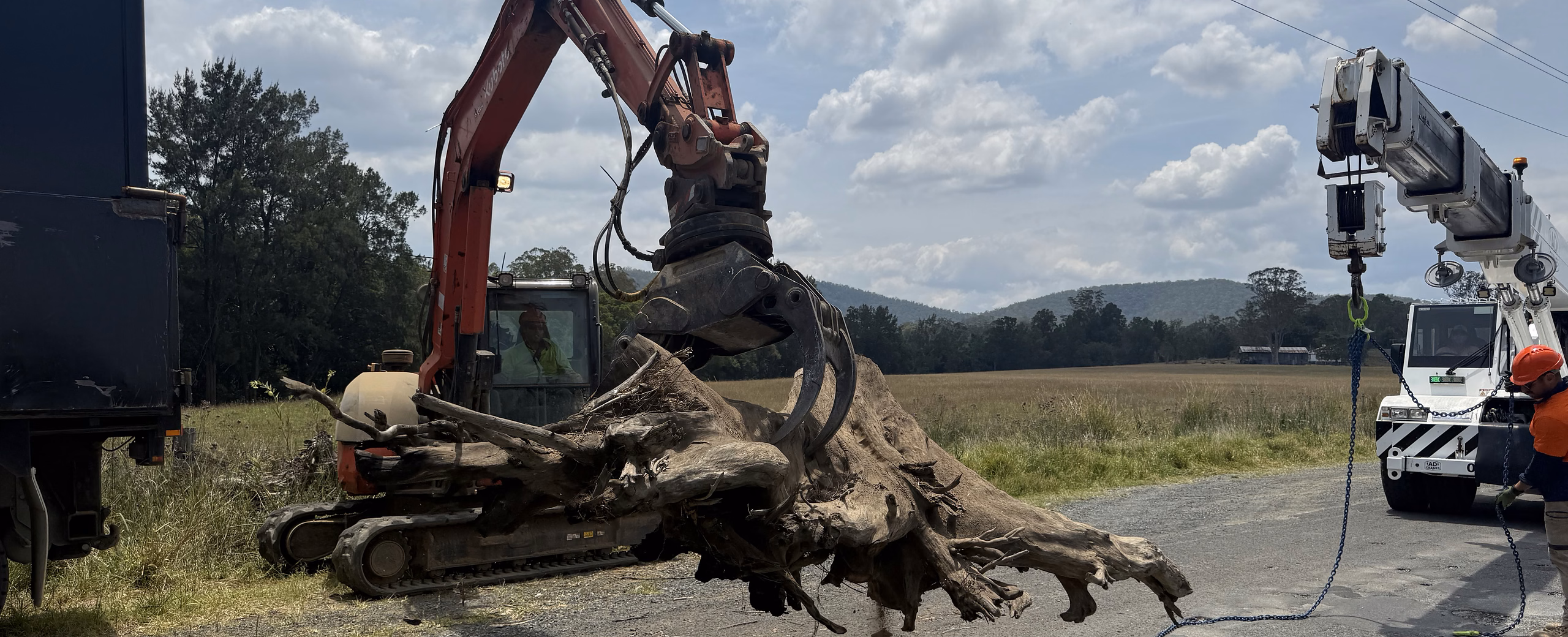 Crane and crew lifting flood debris off a rural bridge during a river clean-up