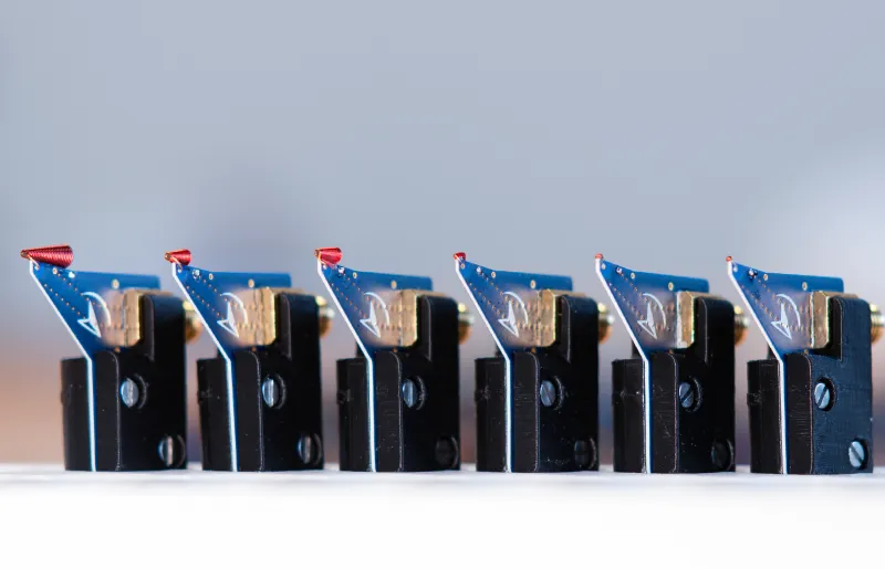 Six identical black and blue electromagnetic injection probe kits with red tips lined up in a row on a white surface.