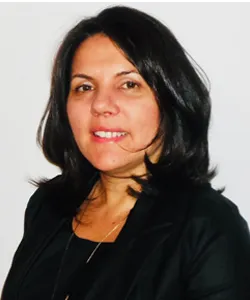 Portrait of a woman with shoulder-length dark hair wearing a black jacket and a necklace, smiling slightly against a white background.