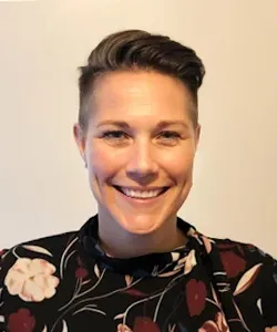 Smiling person with short dark hair wearing a black floral-patterned top against a plain light background.