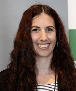 Smiling woman with long curly brown hair wearing a black and white striped top and hoop earrings.