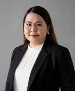 Professional portrait of a woman with long dark hair wearing glasses, a white blouse, and a black blazer against a gray background.