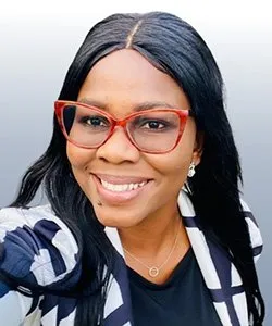 Smiling woman with long black hair, wearing red glasses, a black and white patterned jacket, and a black top.