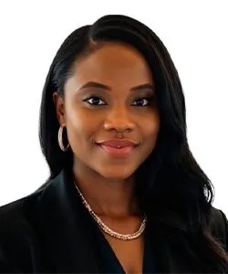 Portrait of a smiling woman with long black hair, wearing hoop earrings, a necklace, and a black blazer.