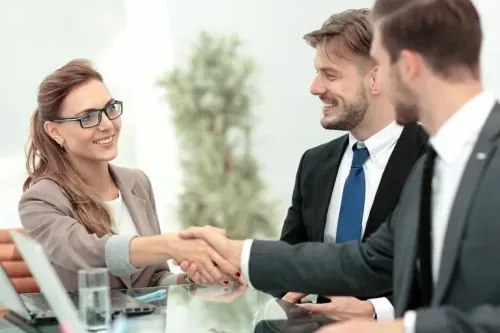 Smiling businesswoman shaking hands with a male colleague across a glass table during a meeting.
