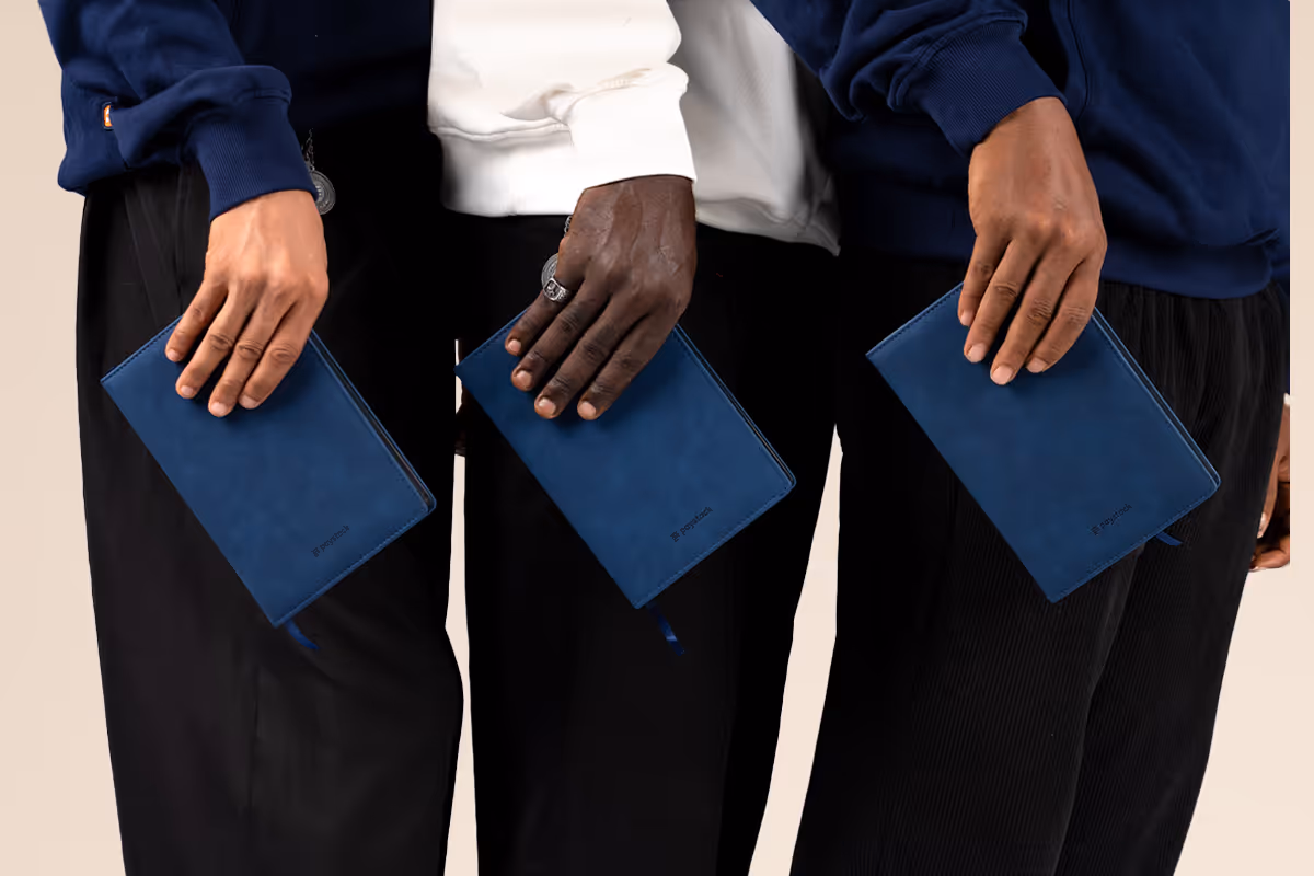 Three people holding identical blue leather notebooks, each against their black pants.
