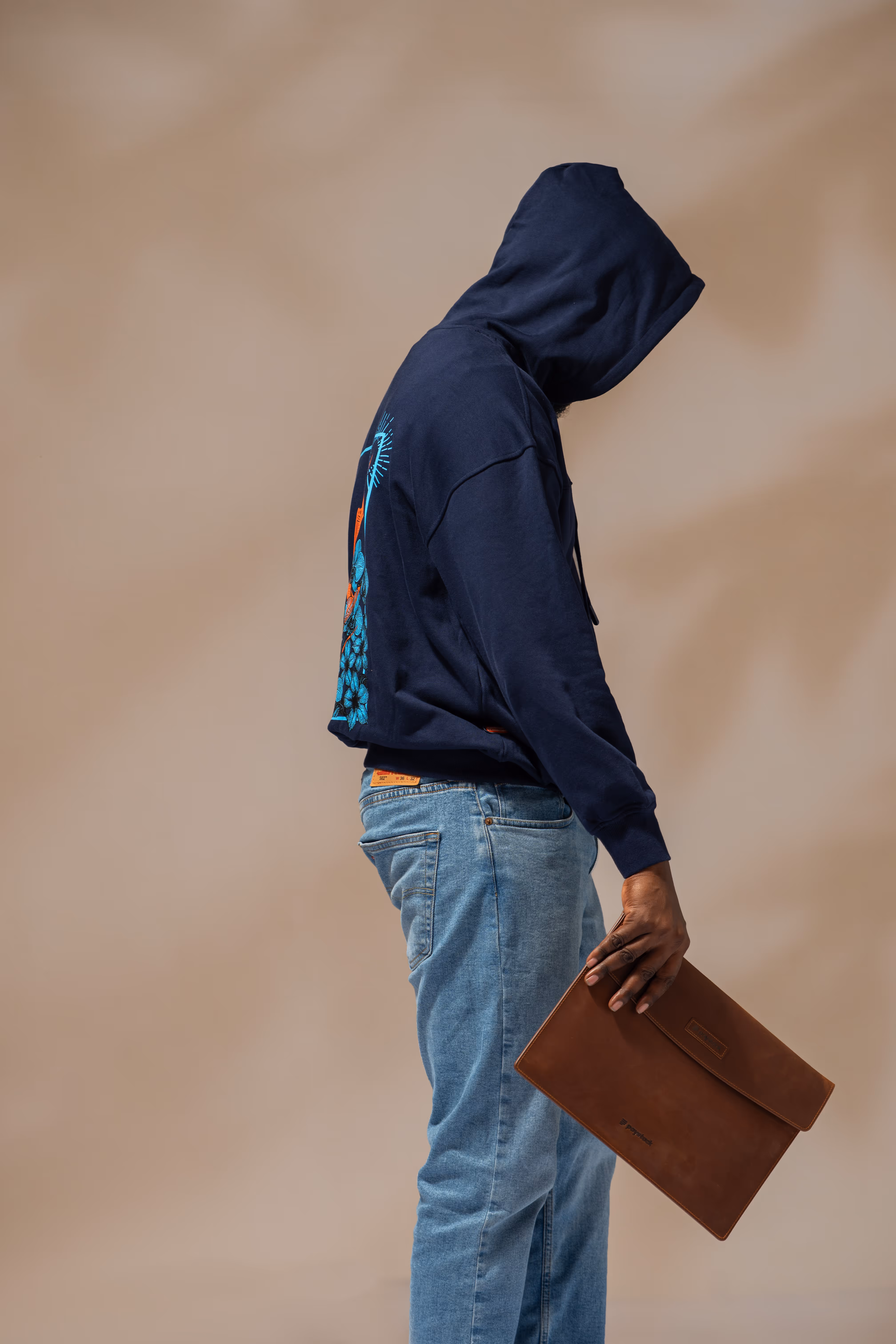 Person in blue hoodie with graphic on back and light blue jeans holding a brown leather portfolio folder.