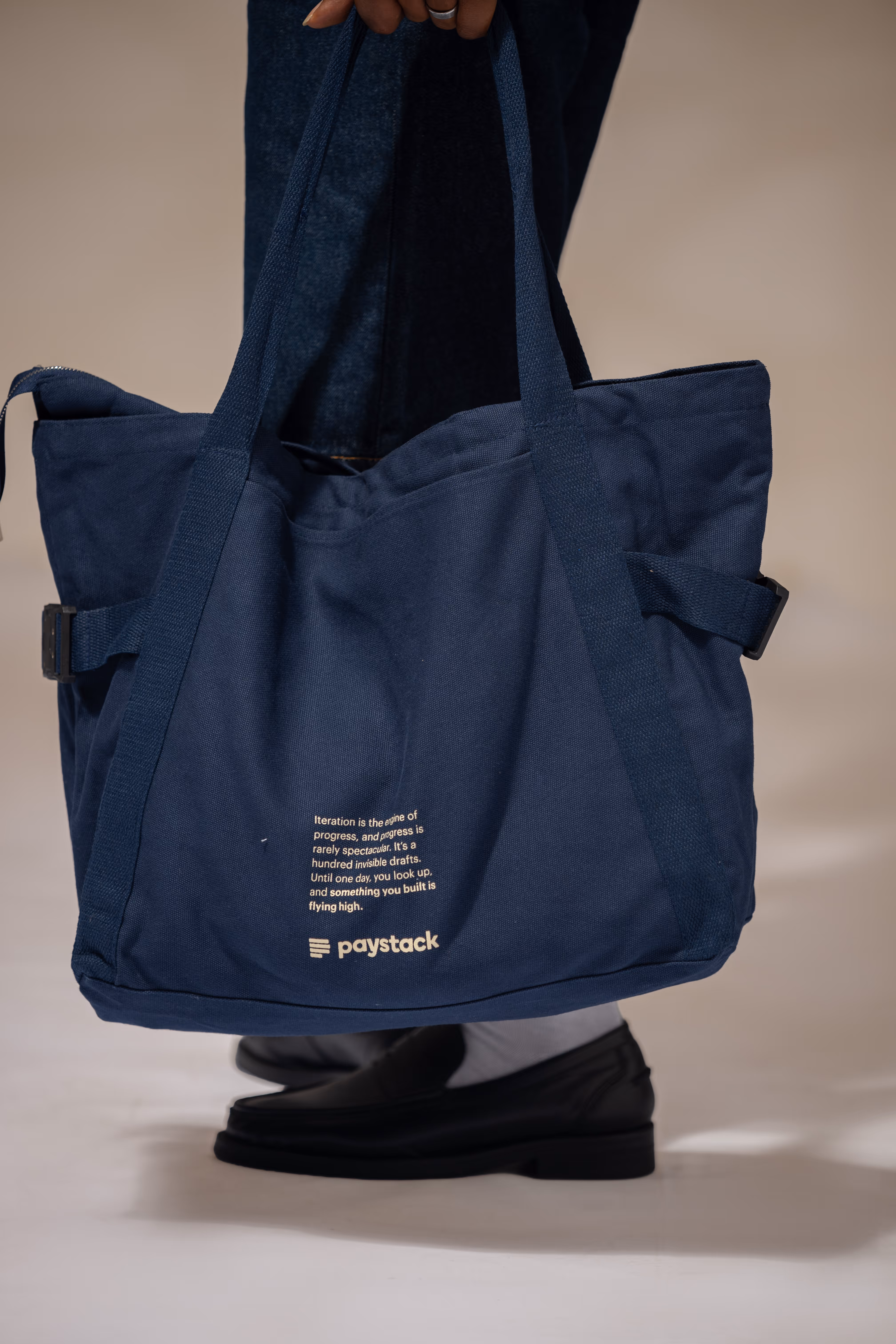 Person holding a navy blue tote bag with the Paystack logo and motivational text.