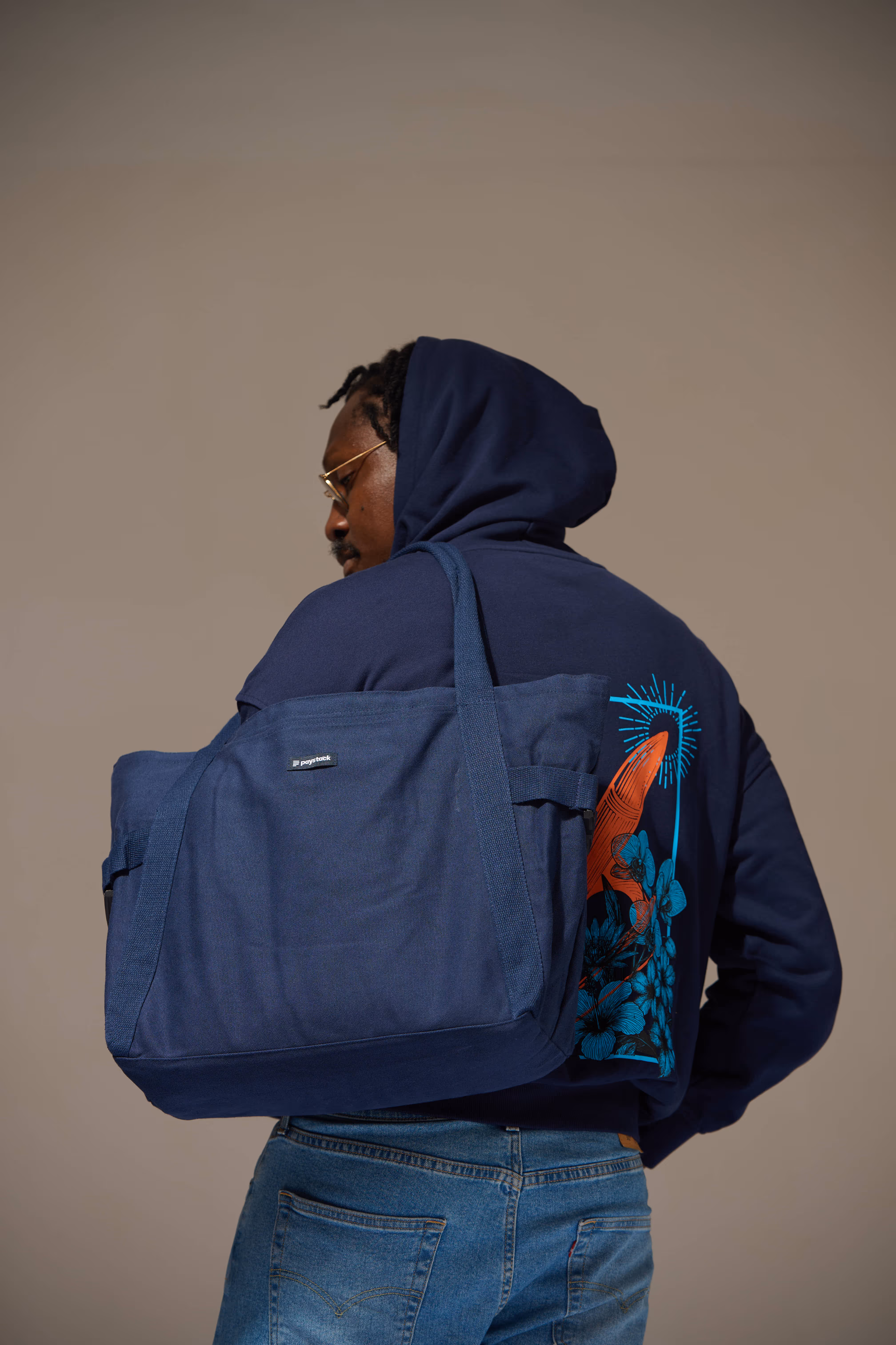 Man wearing a navy hoodie with a red and blue graphic and carrying a large navy blue tote bag over his shoulder.