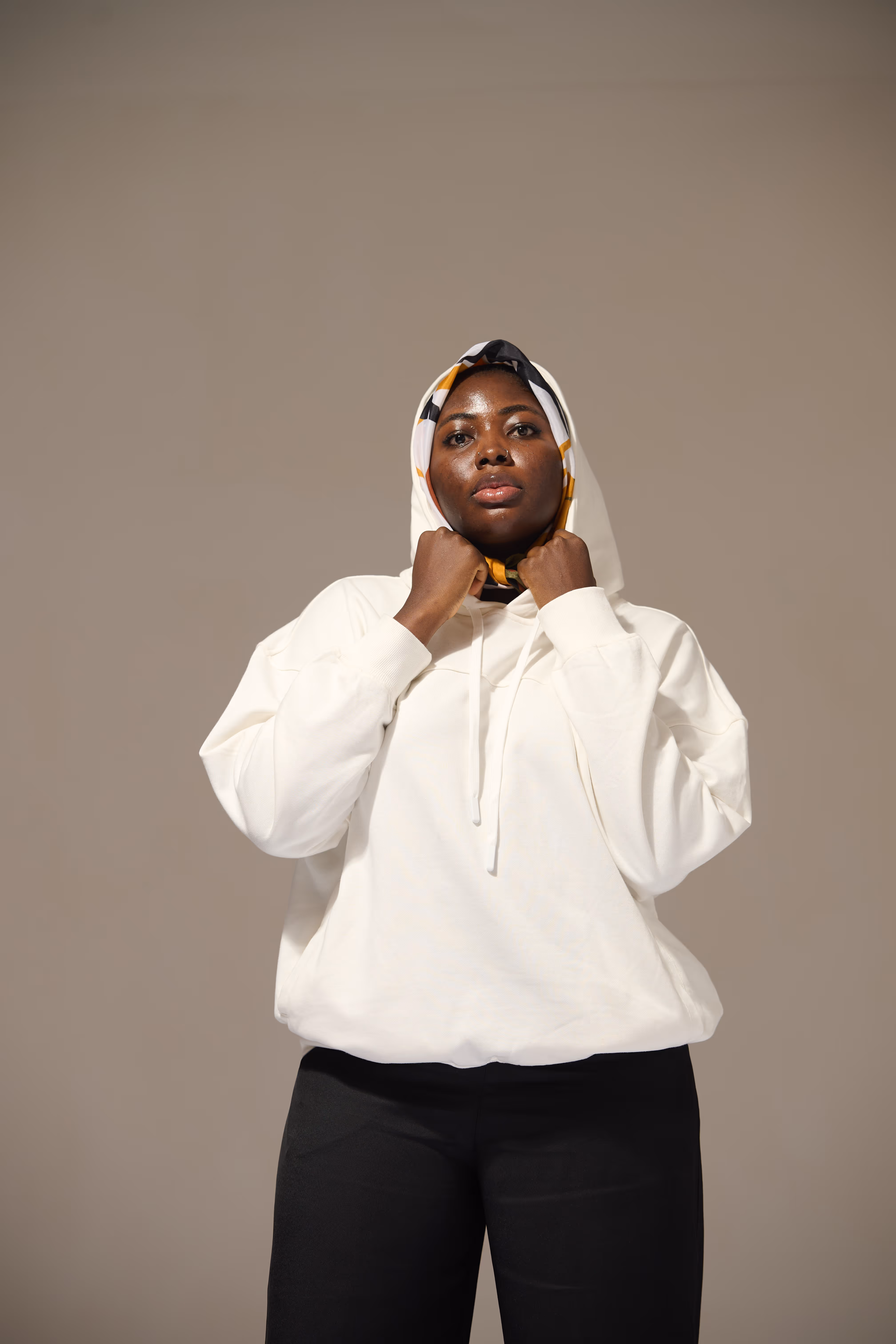 Confident woman wearing a white hoodie and a patterned headscarf holding the hoodie strings.