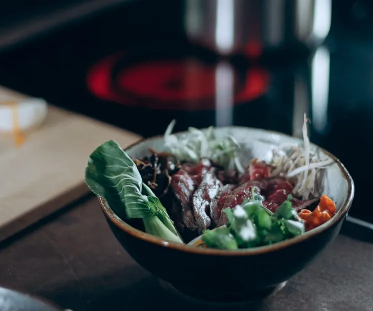 Bol de bibimbap avec des légumes, des pousses, et de la viande tranchée sur une table de cuisine.
