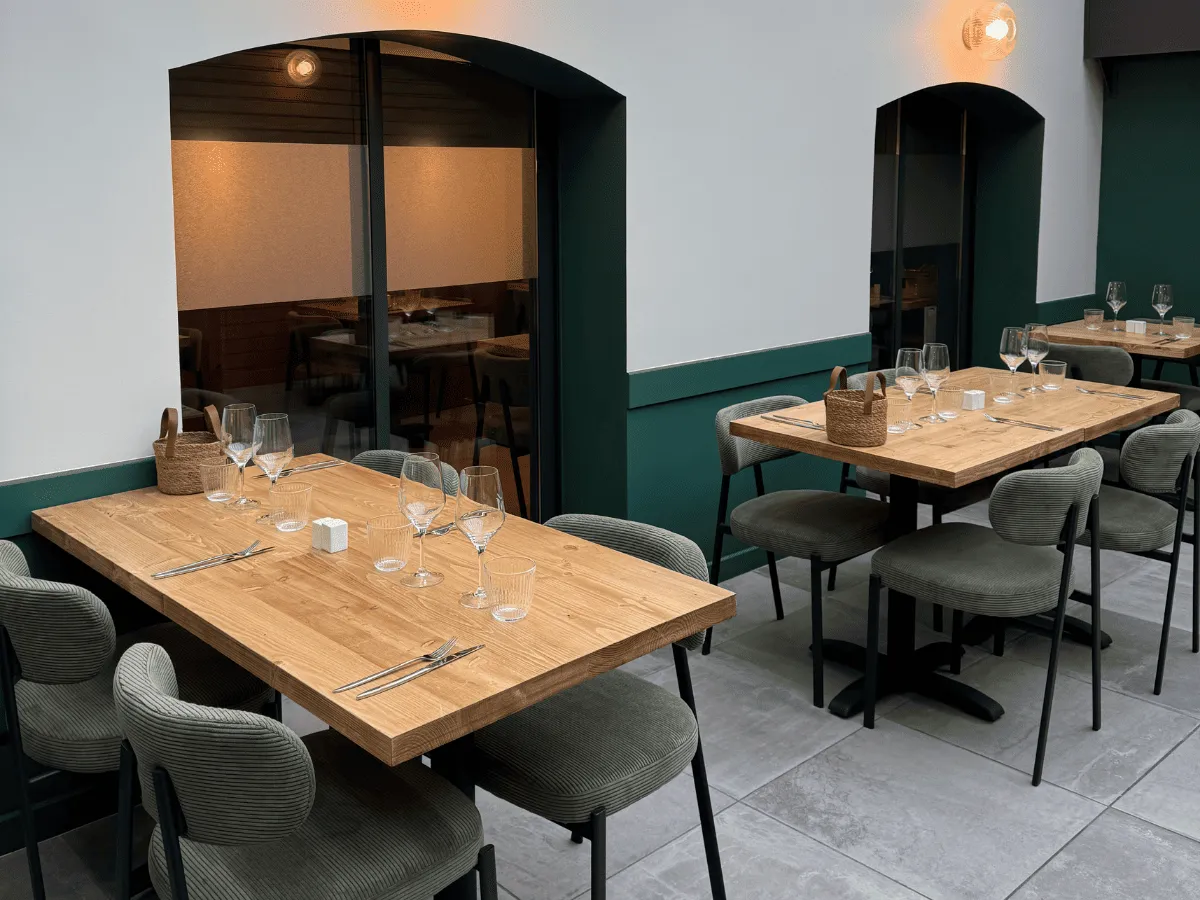 Salle de restaurant moderne avec tables en bois, chaises grises et verres à vin alignés.