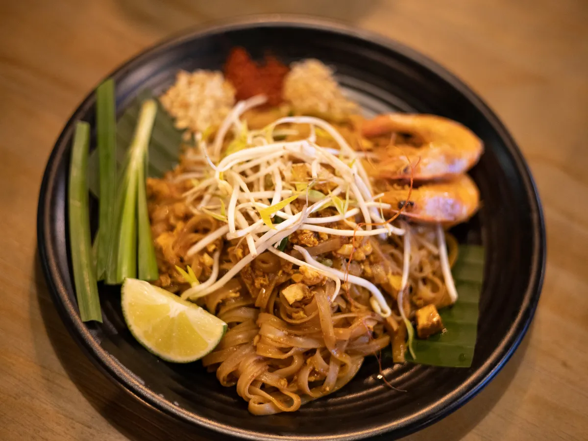 Assiette de pad thaï aux crevettes avec germes de soja, citron vert, et oignons verts sur une assiette noire meicha cysoing