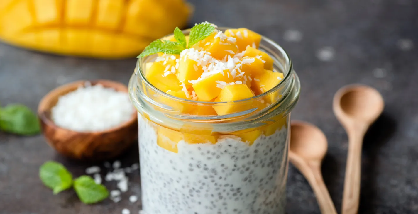 Pudding de graines de chia au lait de coco, garni de dés de mangue et de noix de coco râpée dans un bocal en verre.