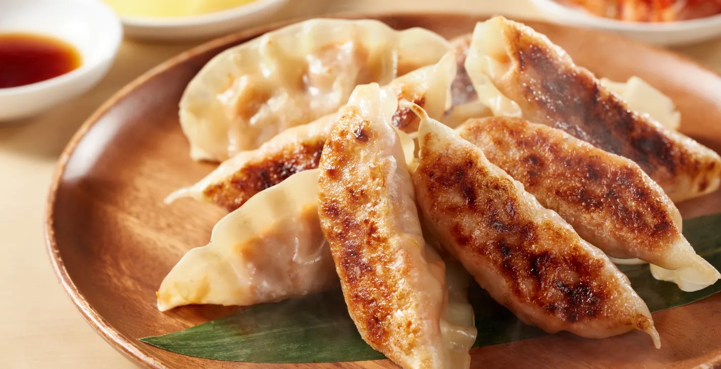 Petits raviolis grillés croustillants servis sur une assiette en bois avec une feuille verte en dessous.