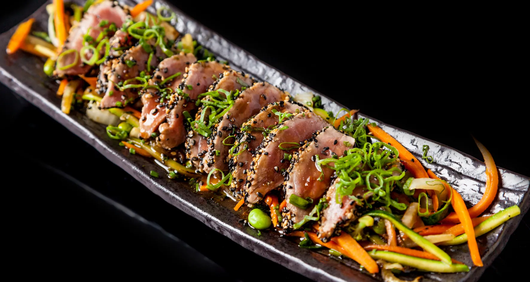 Tranches de thon mi-cuit avec graines et légumes julienne garnies d'oignons verts.