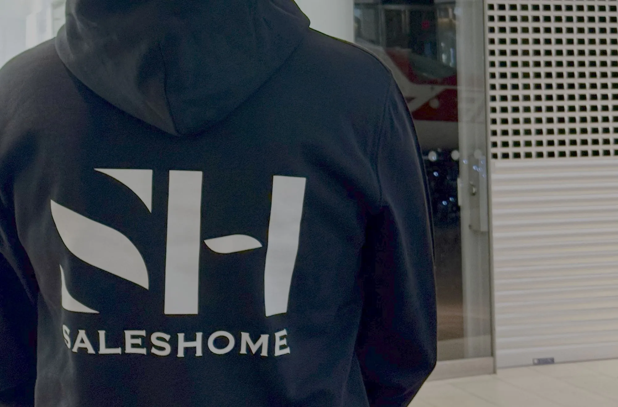 Myyjän selässä musta huppari, jossa iso SH Saleshome -logo.