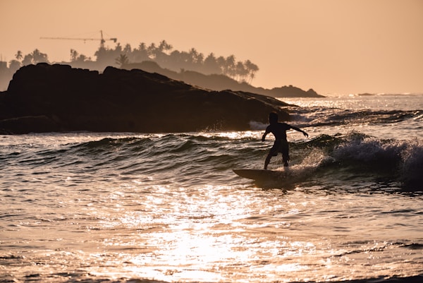 silhouette of person surfing on sea during sunset