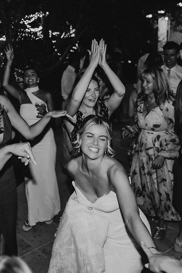 Bride in a wedding dress dancing joyfully with guests in a lively celebration.