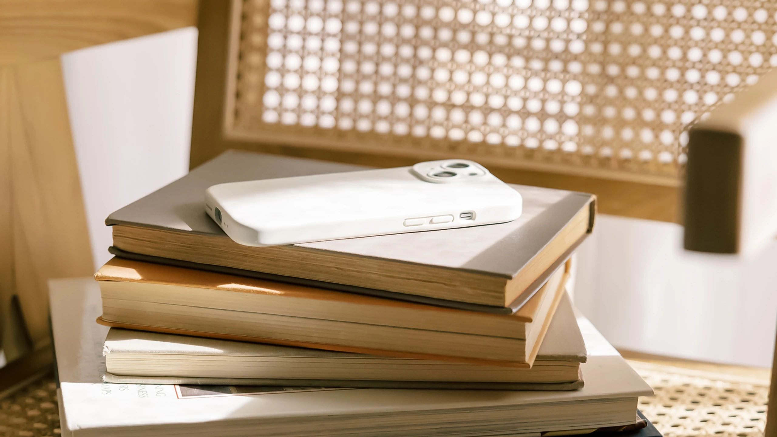 White smartphone with a case resting on a stack of books on a chair with a woven back.