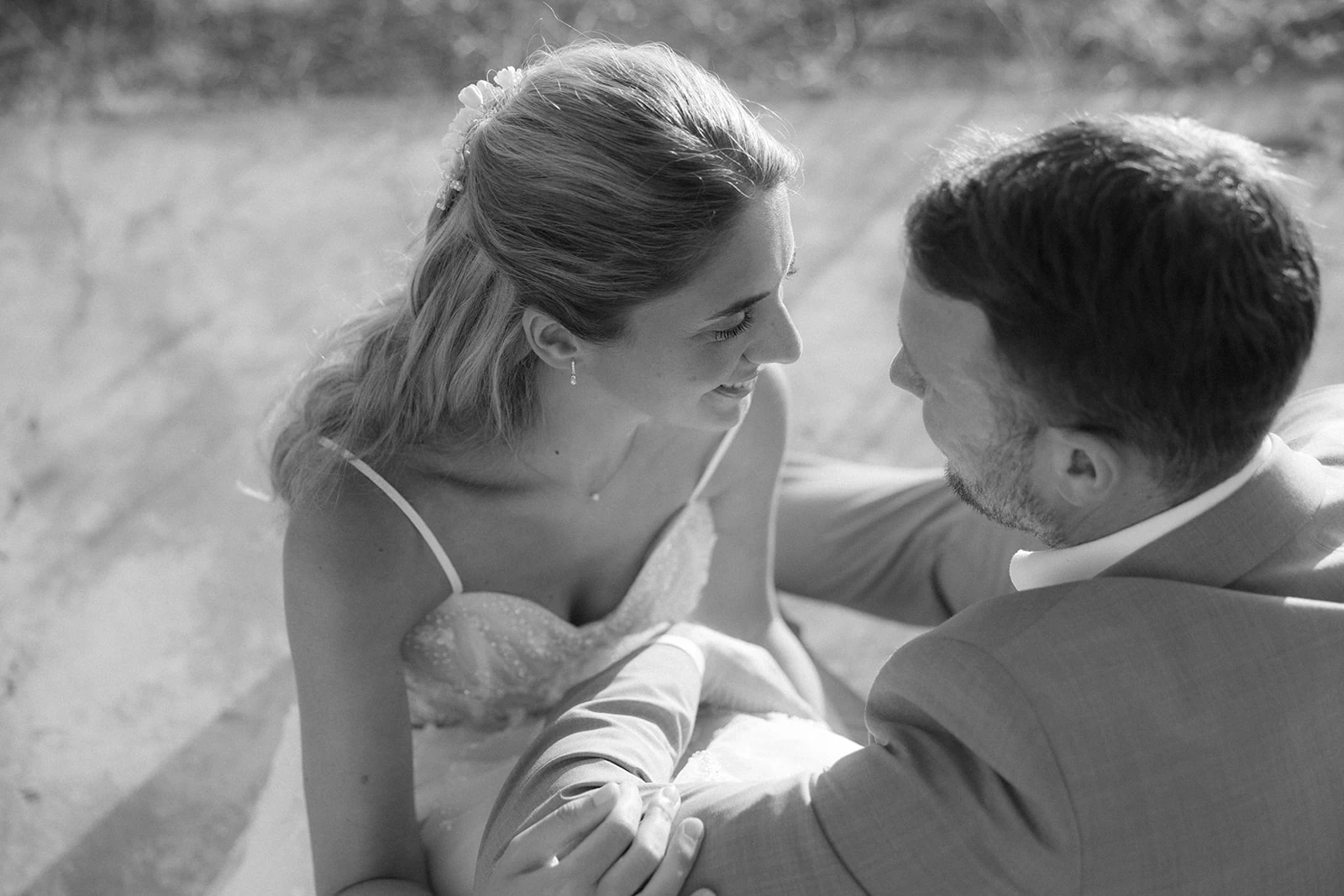 Black and white photo of a bride and groom sitting closely, smiling and looking into each other's eyes.