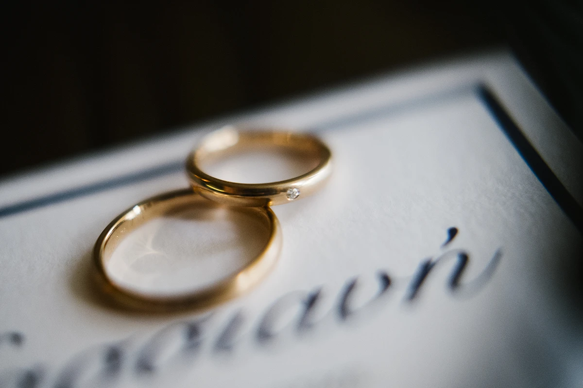 Two gold wedding rings, one with a small diamond, resting on a card with calligraphy text.