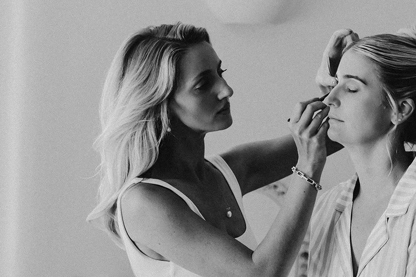 Makeup artist applying eyeshadow on a woman's eyelid in a black and white photo.