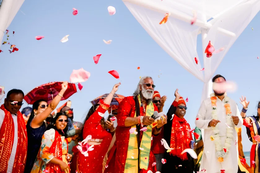Group of people dressed in traditional Indian attire celebrating by throwing flower petals outdoors.