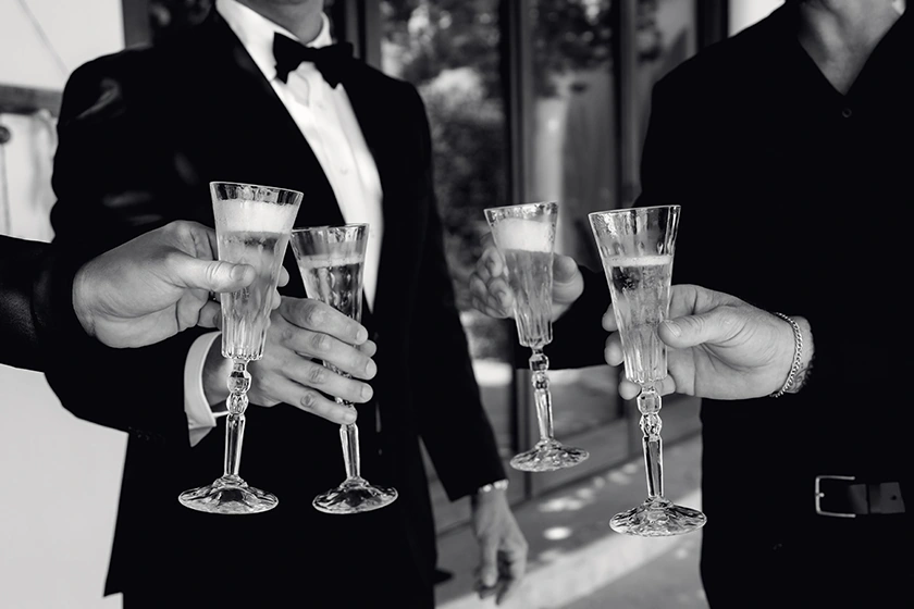 Four men in formal attire holding champagne flutes in a toast.
