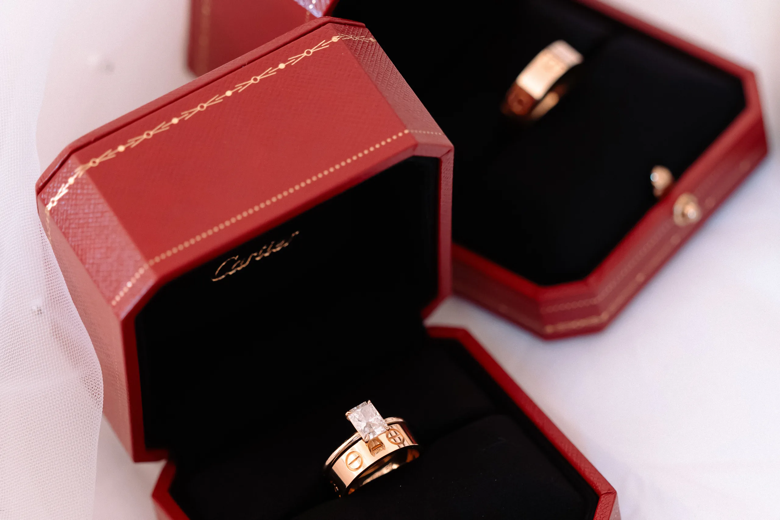 Two Cartier rings in red jewelry boxes with black velvet interiors on a white surface.