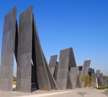 Abstract concrete monument with tall, angular vertical slabs against a clear blue sky.