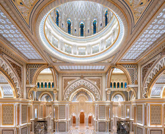 Ornate interior of a palace hall with decorative arches, intricate patterns, and a large illuminated dome ceiling.