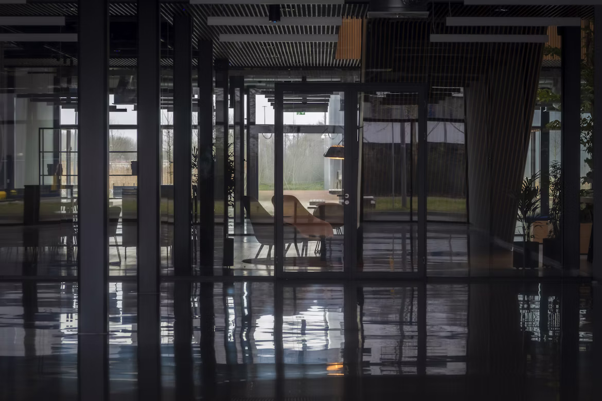 Modern office interior with glass walls, empty chairs, tables, and reflective floor.