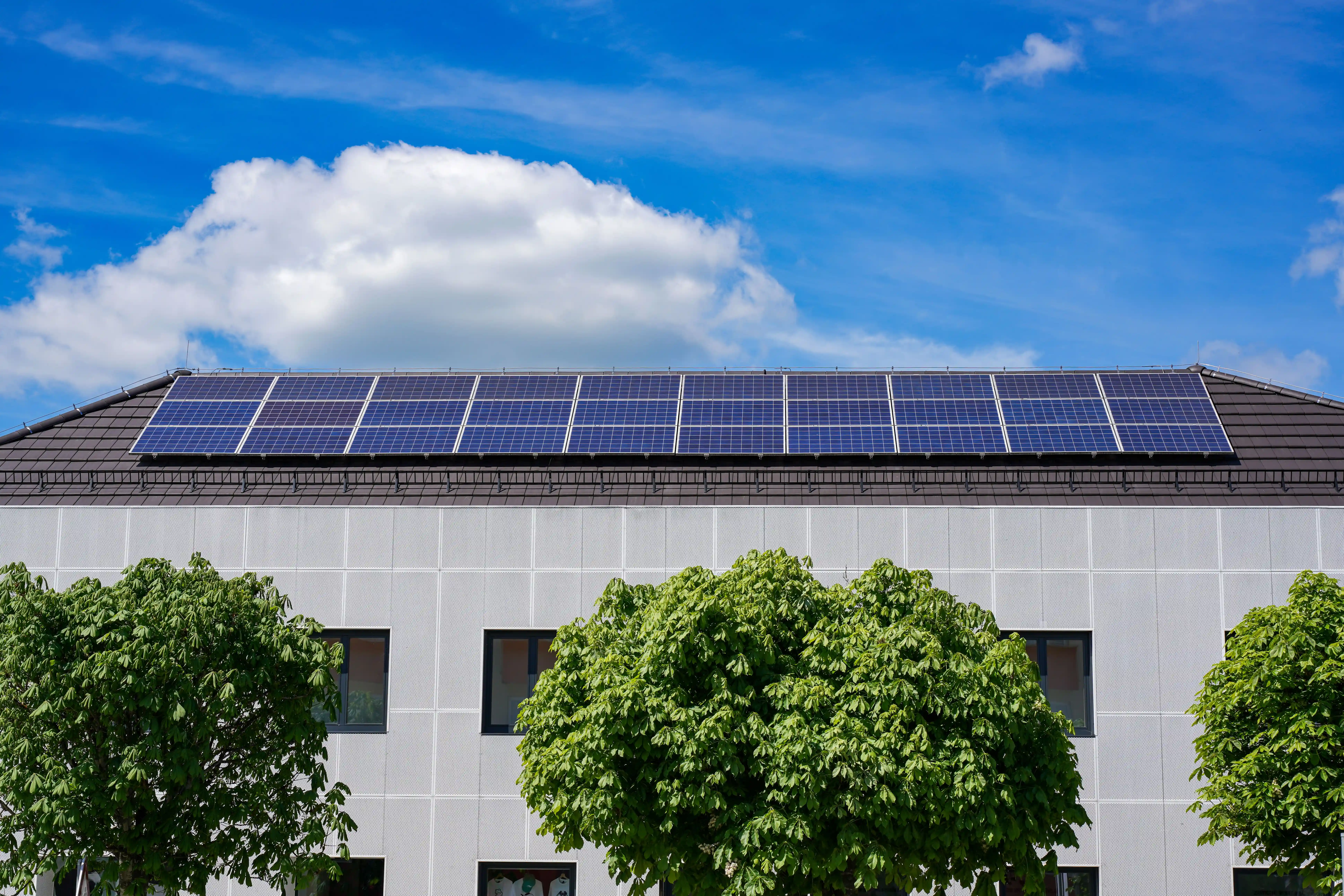 Solar panels installed on the rooftop of a modern building under a blue sky with clouds.