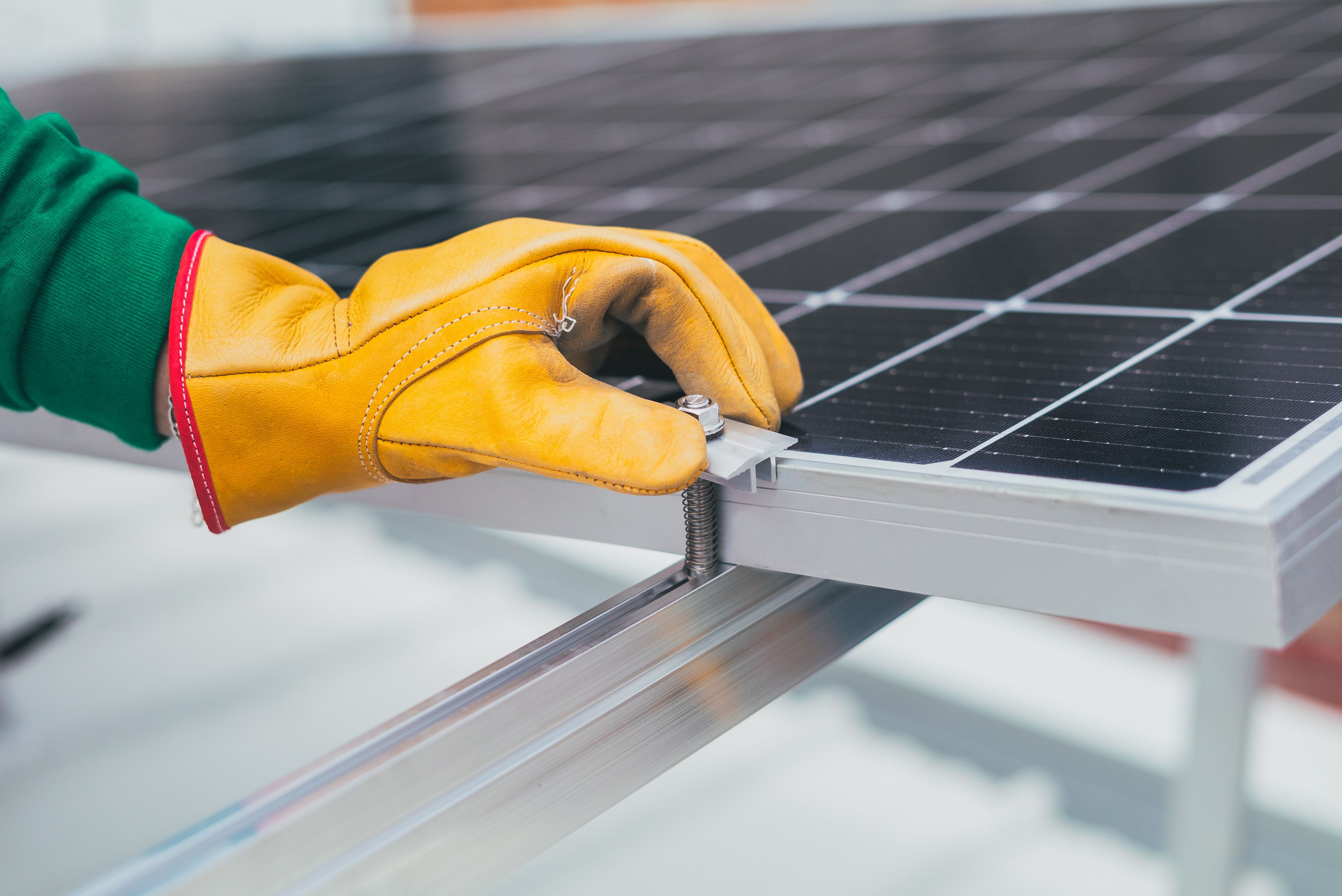 Gloved hand fastening a solar panel to a metal frame with a bolt and spring clamp.