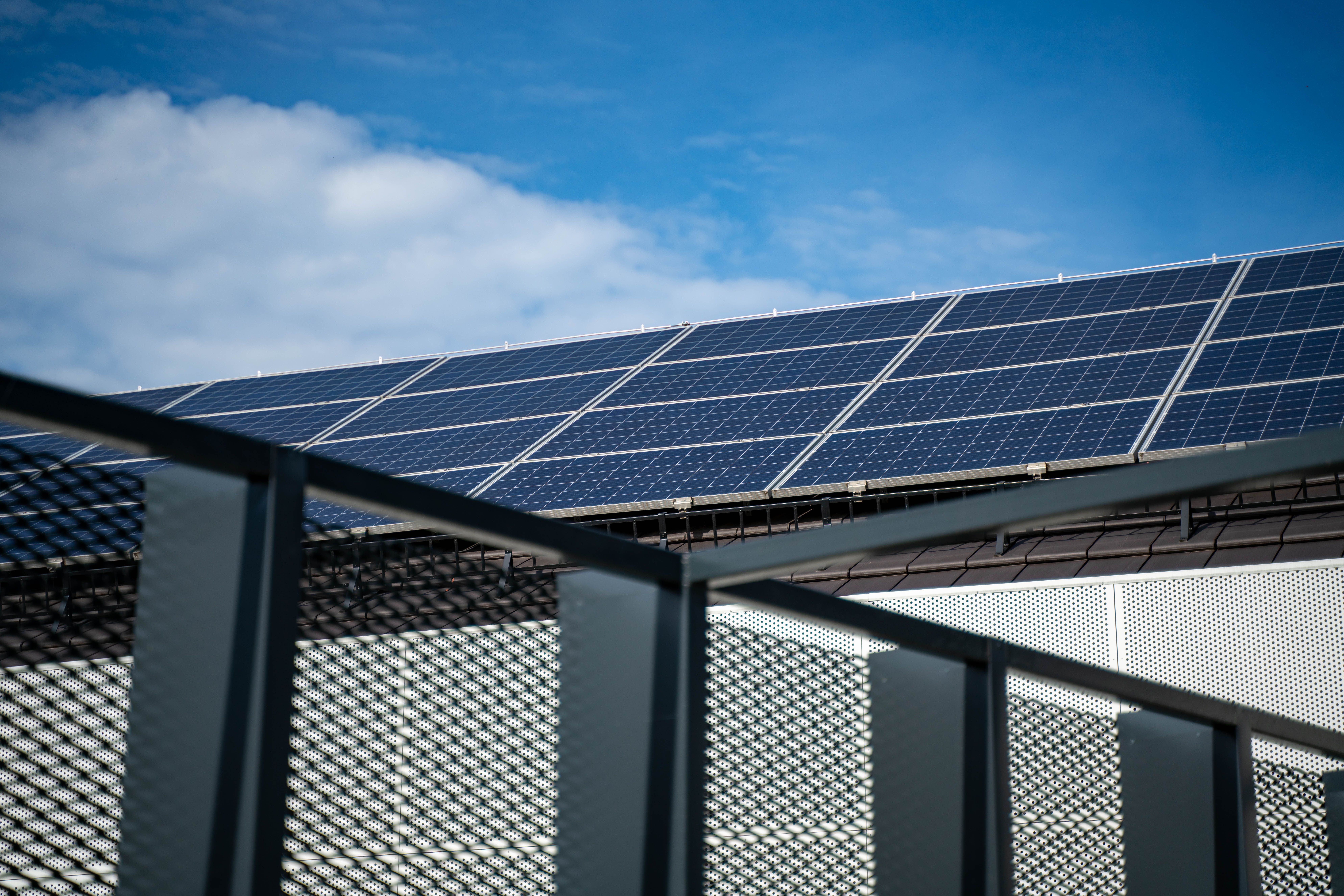 Solar panels installed on a rooftop under a partly cloudy blue sky with a metal railing in the foreground.