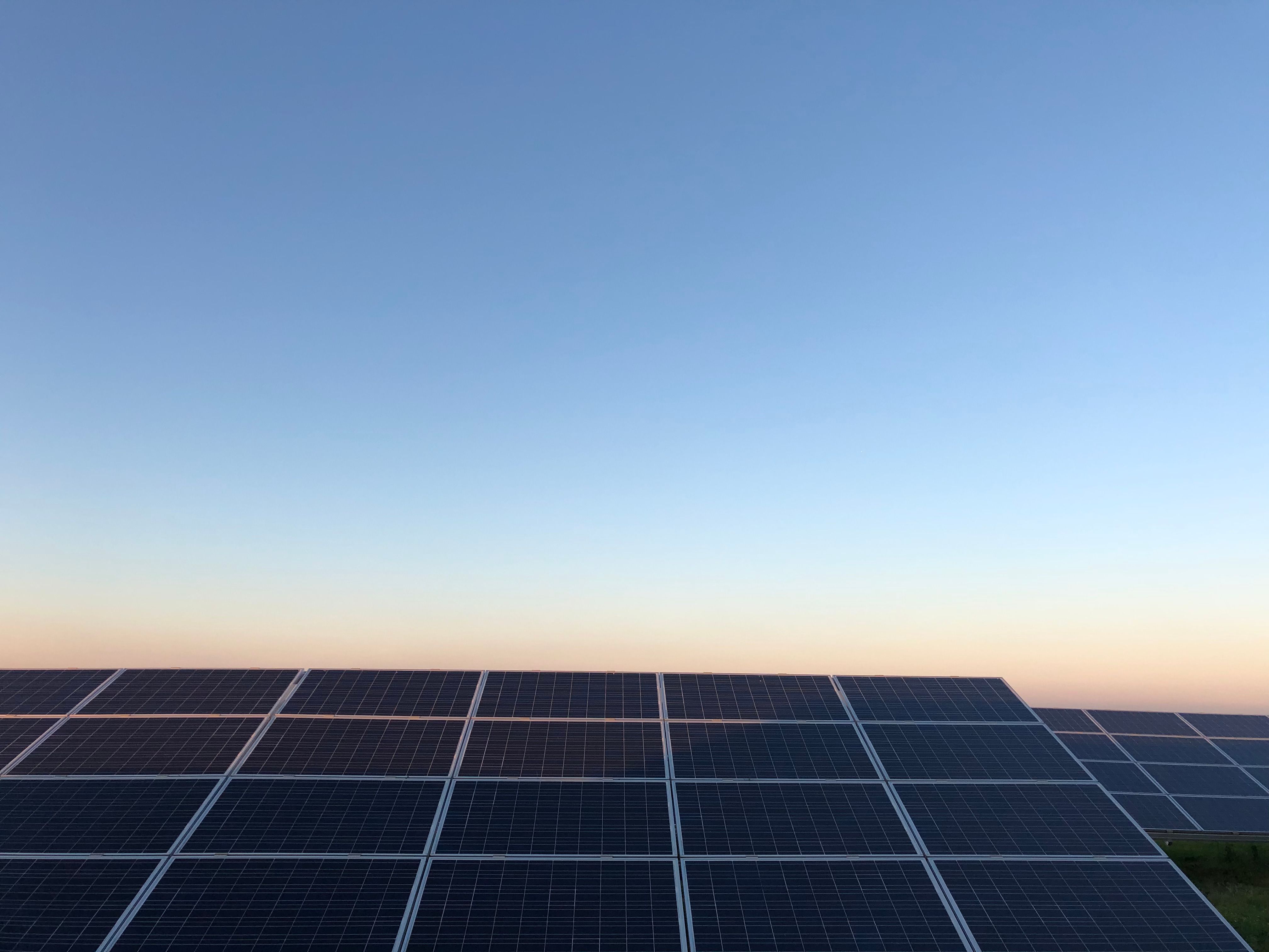 Solar panels angled under a clear sky at sunset with a gradient from blue to soft orange near the horizon.