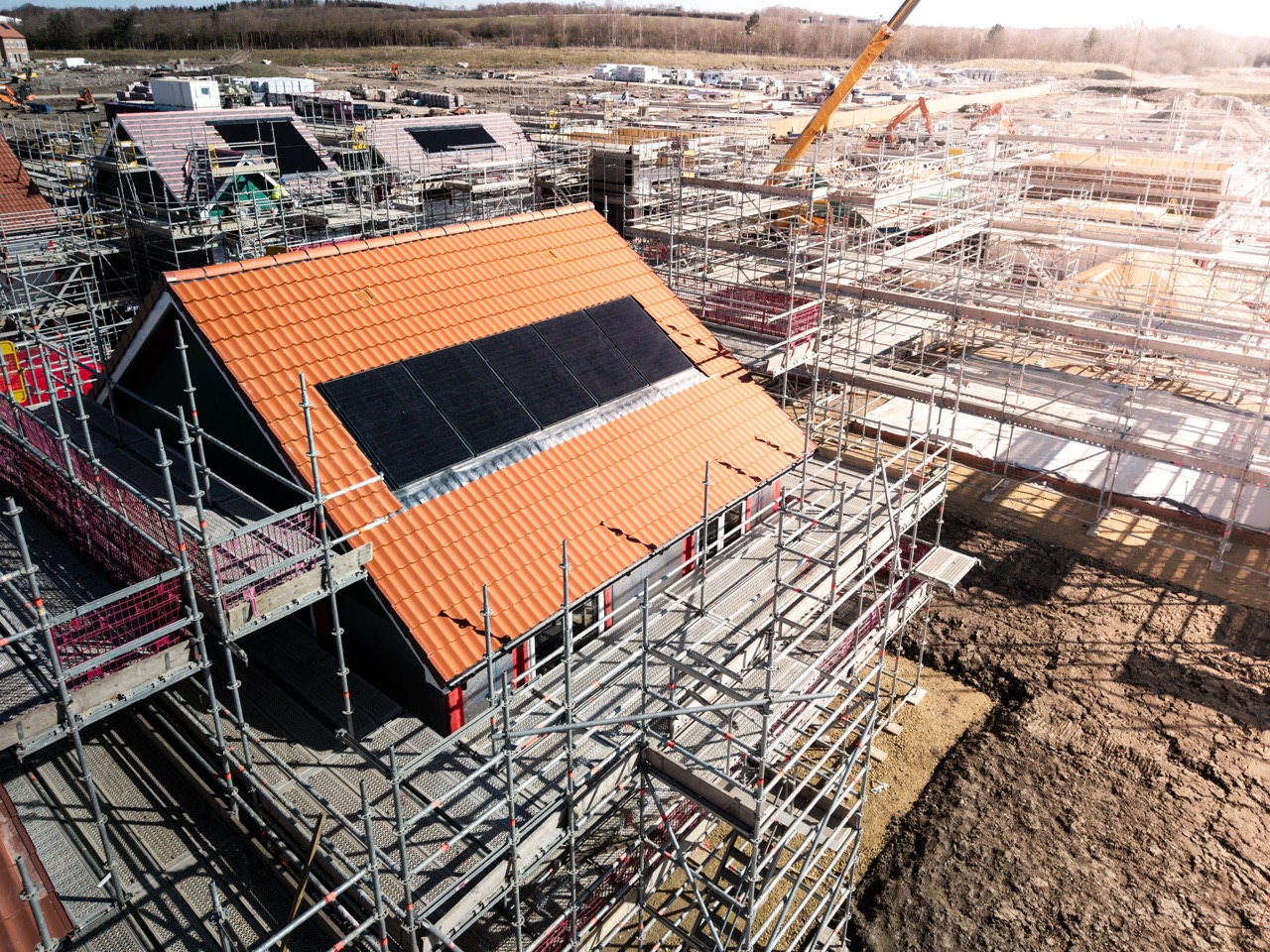 New homes under construction with scaffolding and solar panels installed on tiled roofs.