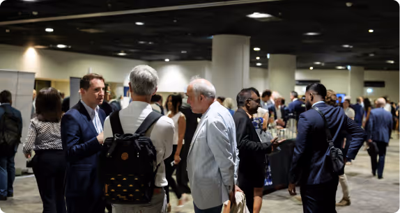 Des personnes en tenue professionnelle discutent lors d'un événement en intérieur avec un grand nombre de participants.