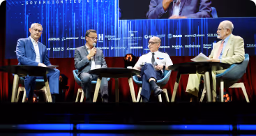 Quatre hommes assis sur scène lors d'un panel de discussion devant un écran bleu avec logos.